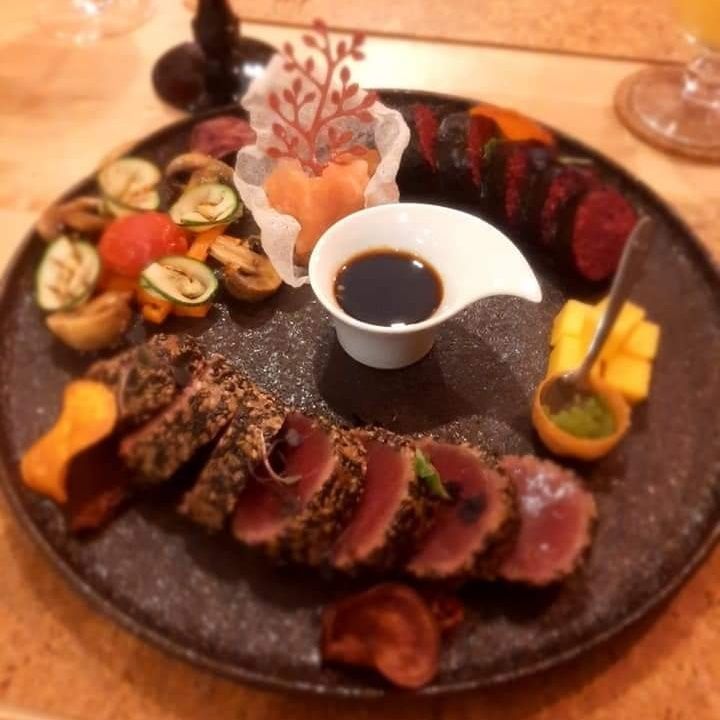 Tataki de atum num prato de pedra escura, com legumes grelhados, sushi e molho de soja.