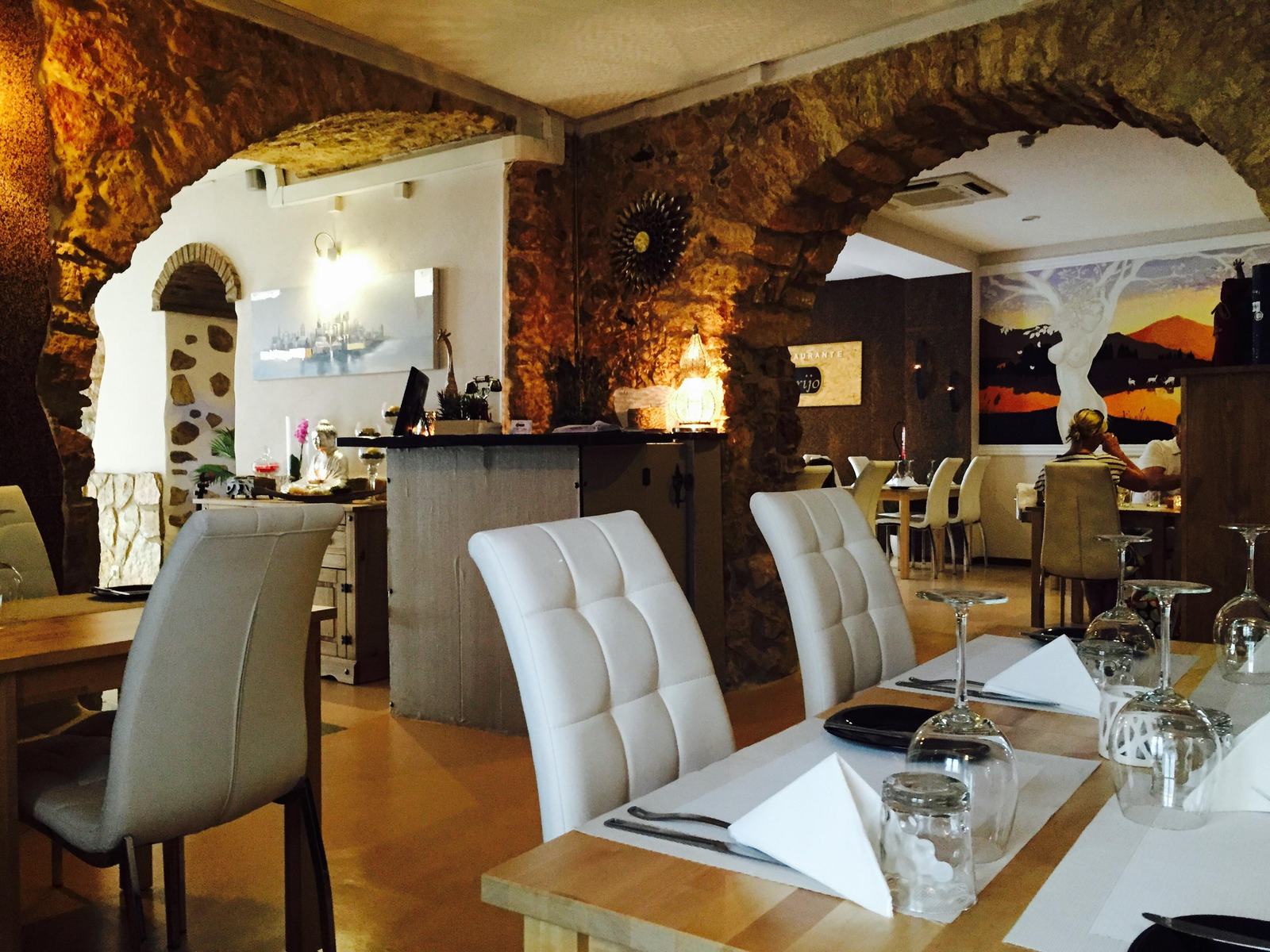 A sala do Ysconderijo: arcos de pedra, paredes brancas, cadeiras brancas e mesas postas.